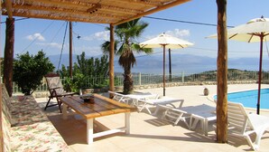 A covered outdoor area with a pool, lounge chairs, and a wooden table.
