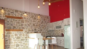 A modern kitchen with stone walls, a dining area with white chairs, and a wooden table.