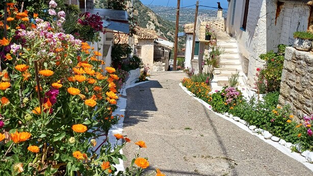 A narrow street lined with colorful flowers and traditional stone buildings.