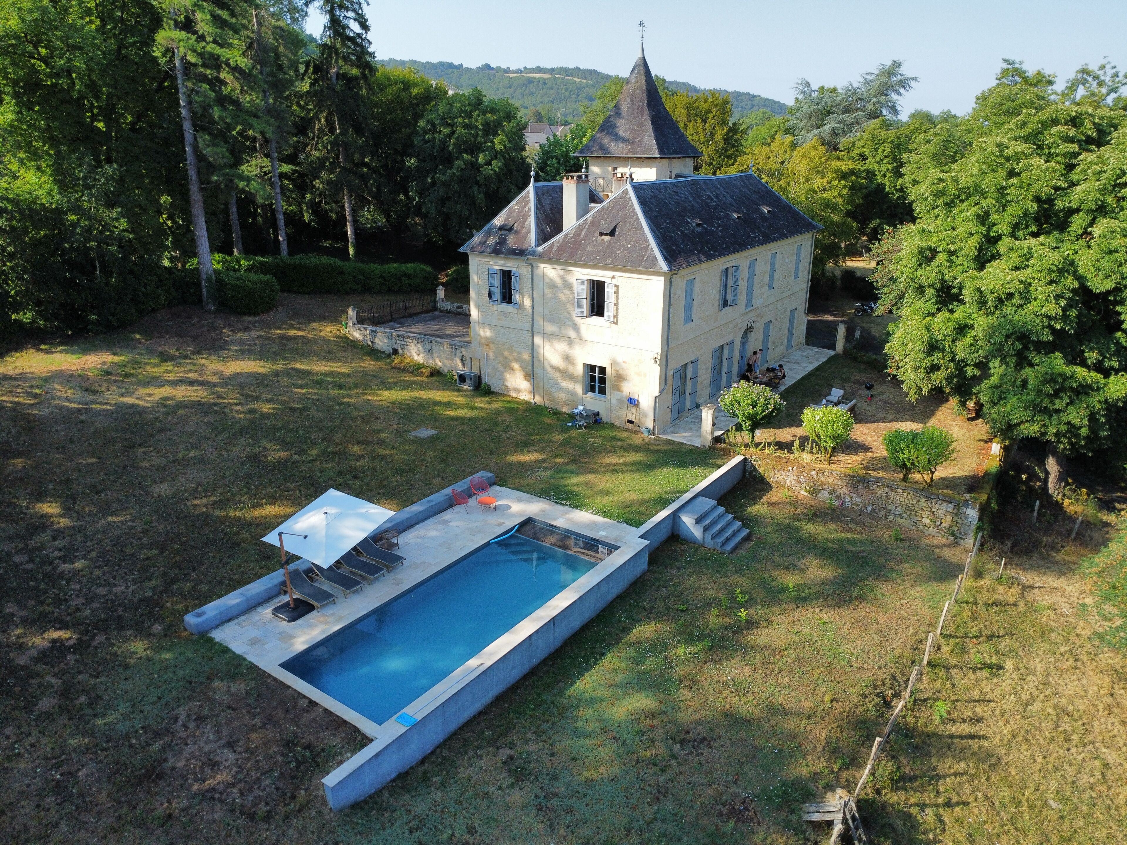 Una casa con piscina, rodeada de árboles y una colina al fondo.