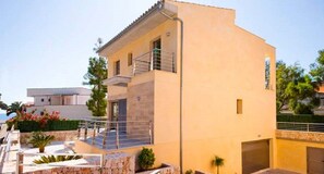 A modern villa with a stone facade, a balcony, and a small garden area.