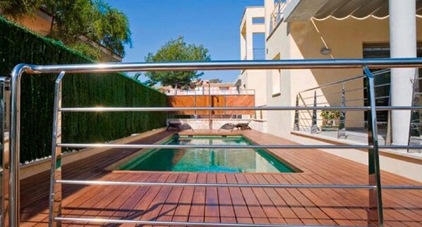 A pool area with a wooden deck, a metal fence, and a building in the background.