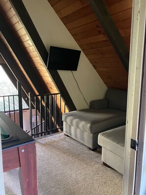 Um quarto de sótão aconchegante, com um sofá, uma TV de tela plana na parede e teto de madeira.