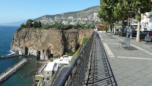 A coastal promenade with a rocky cliff, a metal railing, and a view of the sea. - Sottovoce app.to vicino al mare (Piano di Sorrento)