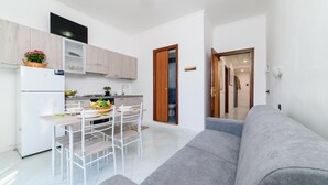 A modern kitchen with white cabinets, a dining table with chairs, and a grey sofa in the living area. - Sottovoce app.to vicino al mare (Piano di Sorrento)