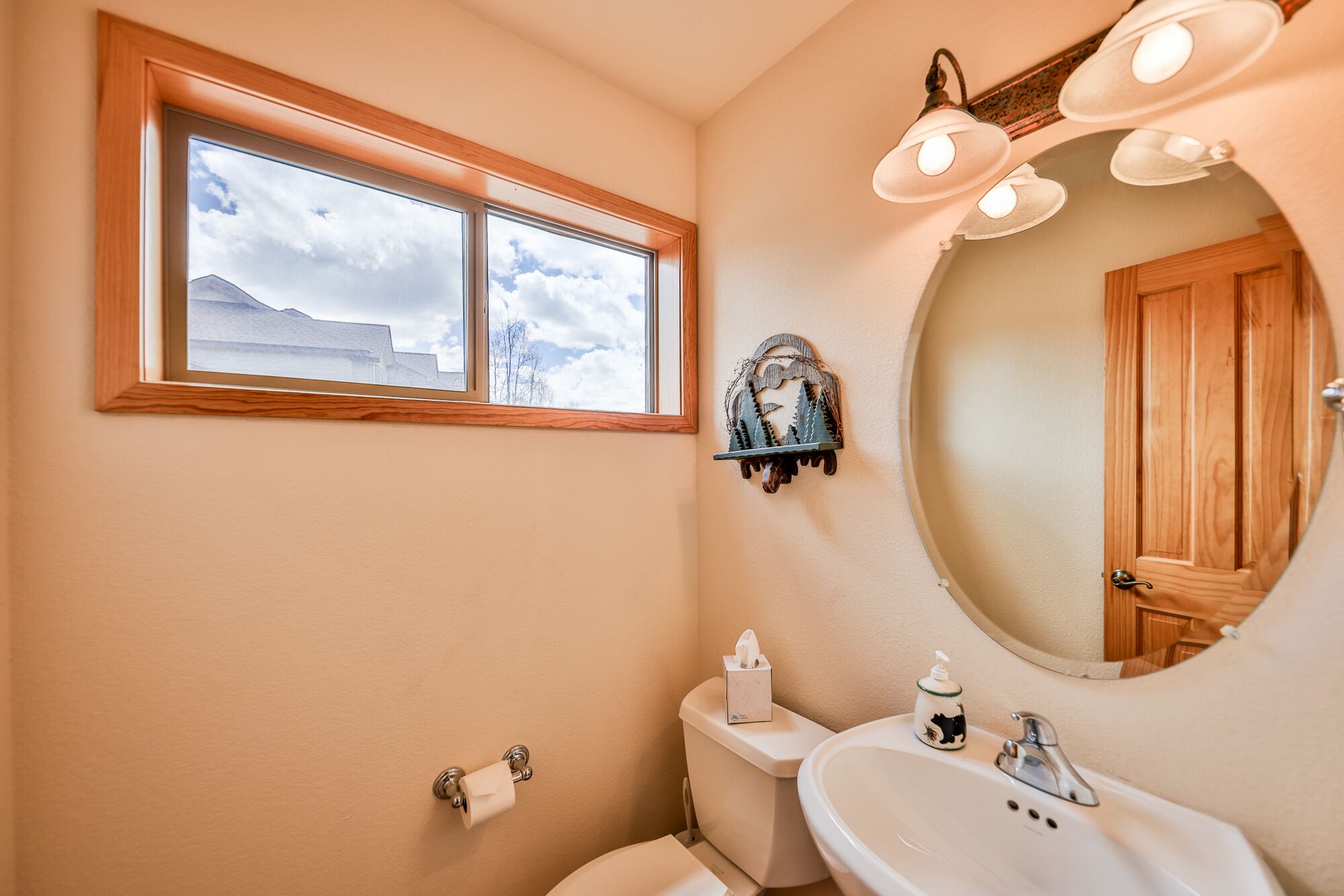 A bathroom with a window, a toilet, a sink, and a mirror.