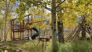 Un parque infantil con tobogán y estructuras para escalar, rodeado de árboles con hojas amarillas.