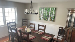 Un comedor con una mesa de madera, sillas, una araña y un cuadro en la pared.