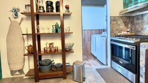A kitchen with a wooden shelf unit, a stove, and a washing machine.