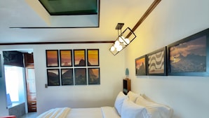 A modern bedroom with a large bed, a skylight, and multiple framed pictures on the wall.