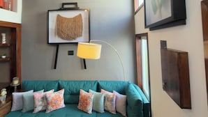 A teal sofa with patterned cushions, a framed artwork on the wall, and a floor lamp.