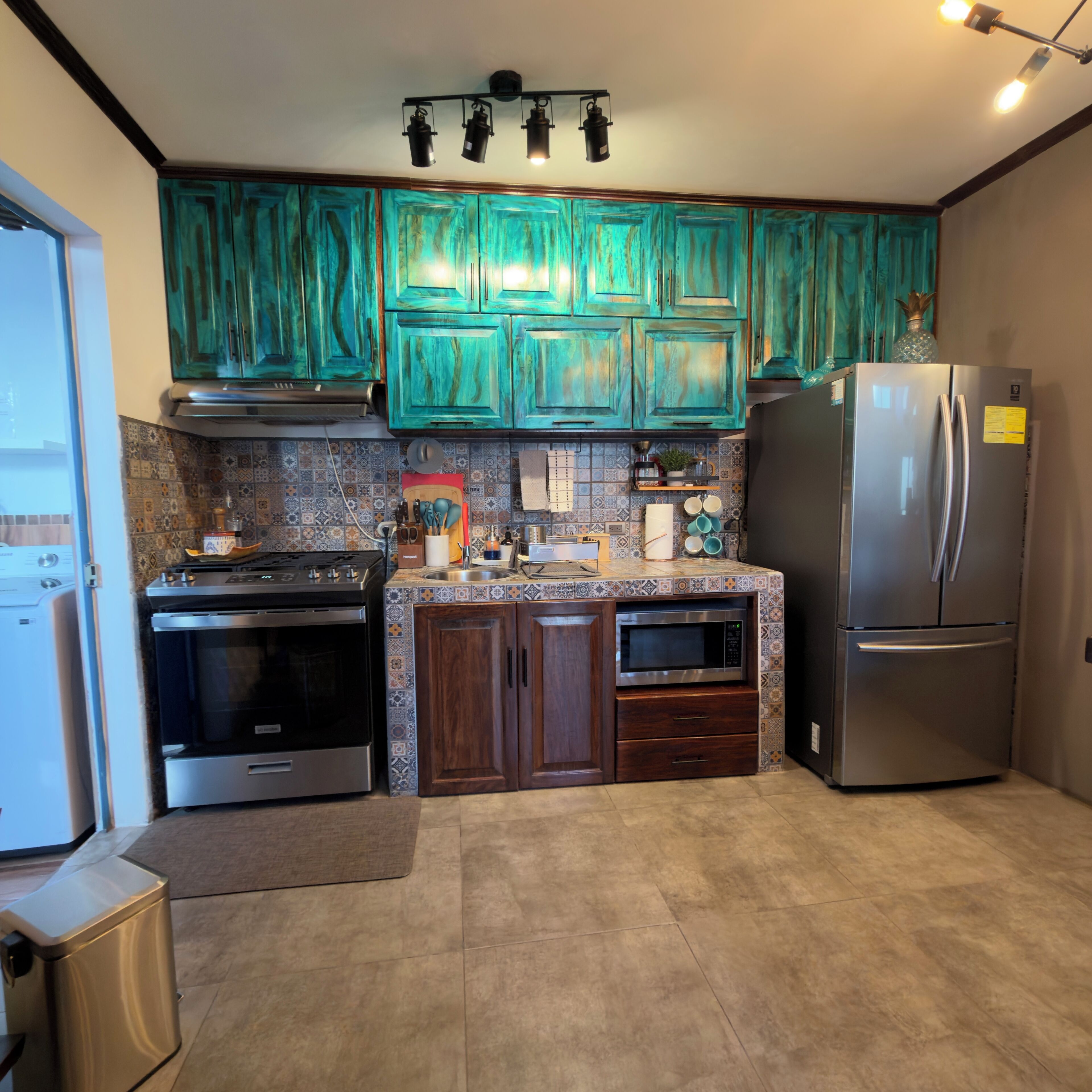 Une cuisine avec des armoires de couleur turquoise, un réfrigérateur en acier inoxydable et une cuisinière.