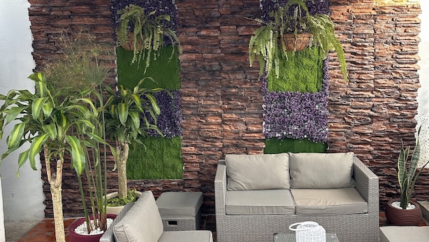 A cozy outdoor seating area with wicker furniture, a stone wall backdrop, and hanging plants.