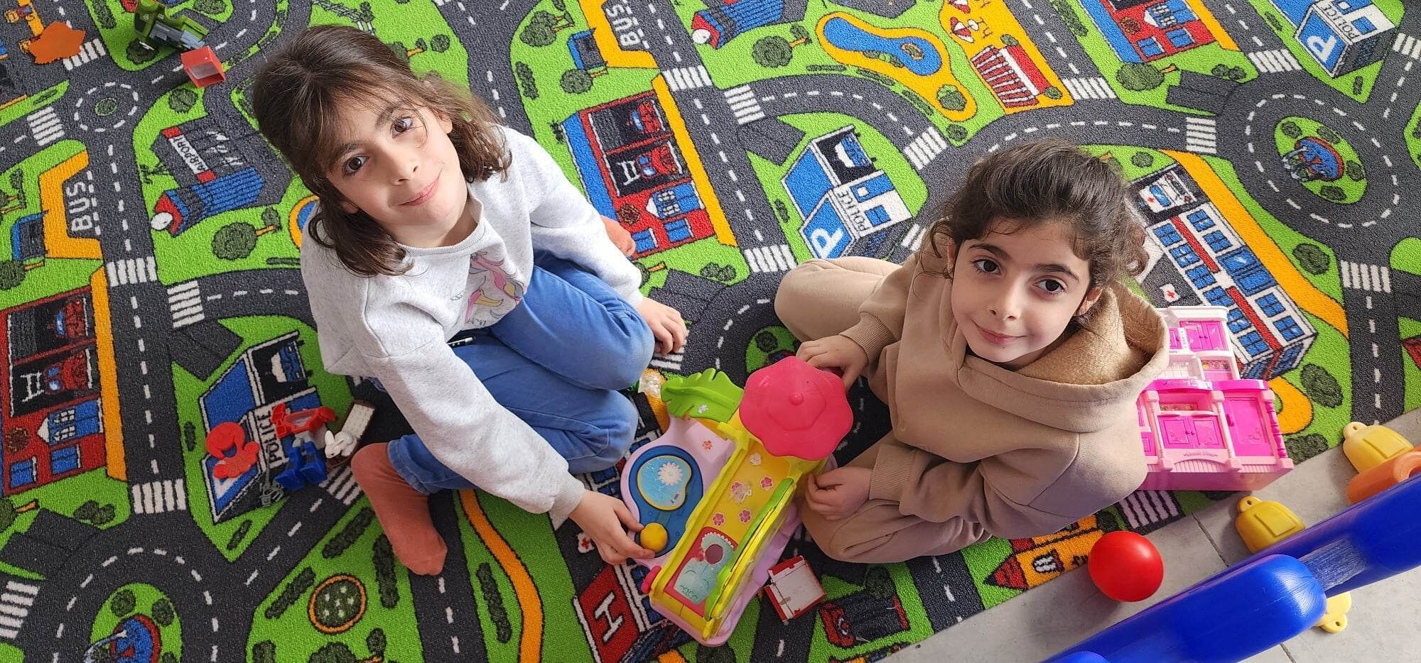 Dos niños jugando con juguetes sobre una alfombra de juego colorida.