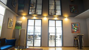 A spacious interior with a high ceiling, large windows, and a seating area with a blue sofa and a small round table. - Mountain Resort Gantiadi (Borjomi)