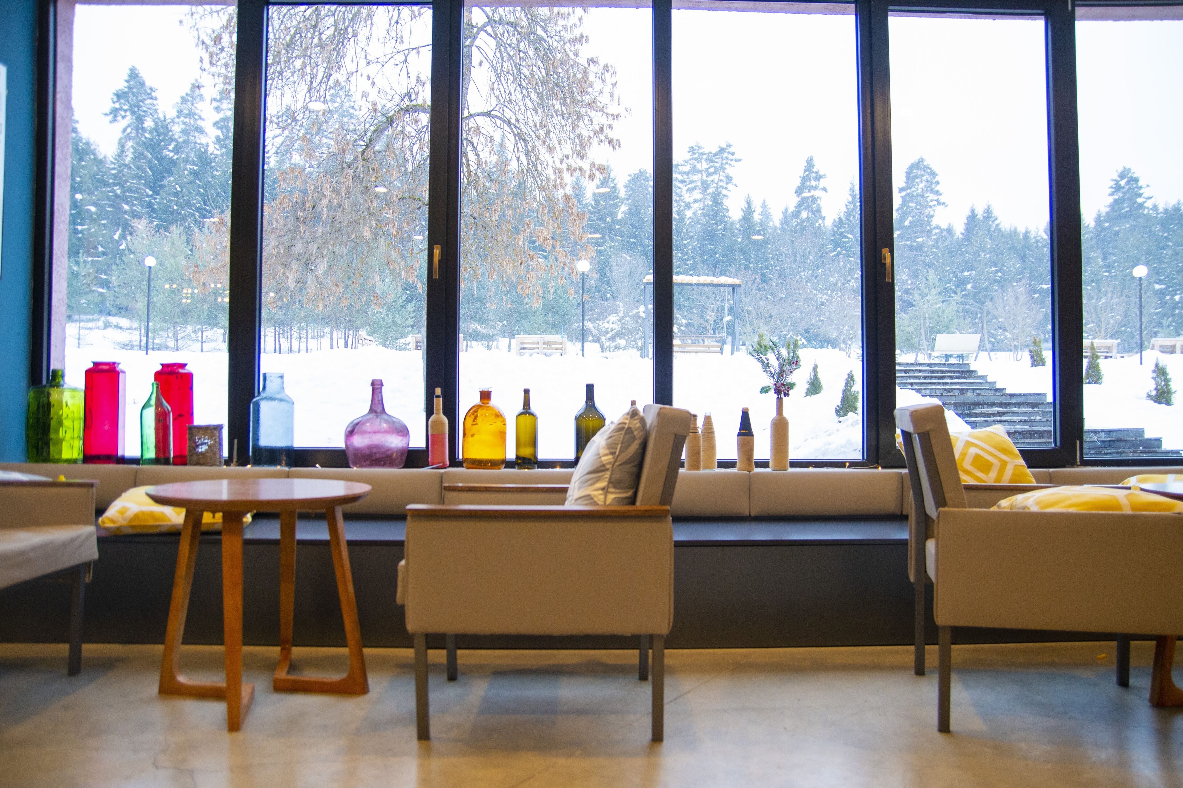 A room with a large window, a sofa, a small table, and colorful bottles on the windowsill.
