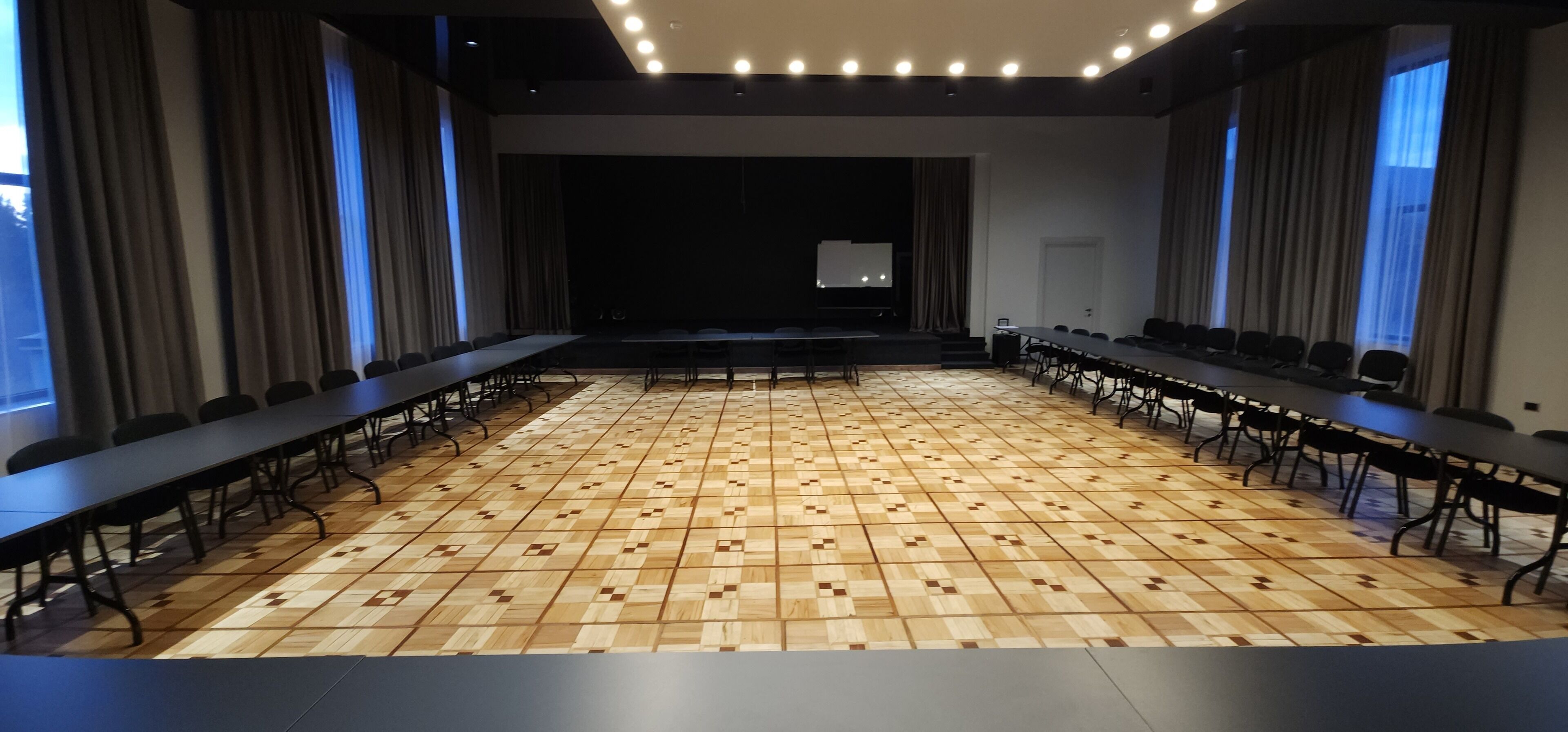 Una sala conferenze con pavimento in legno decorato, lunghi tavoli e sedie.