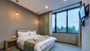 A modern hotel room with a large bed, a TV mounted on the wall, and a window with a view of trees. - Mountain Resort Gantiadi (Borjomi)