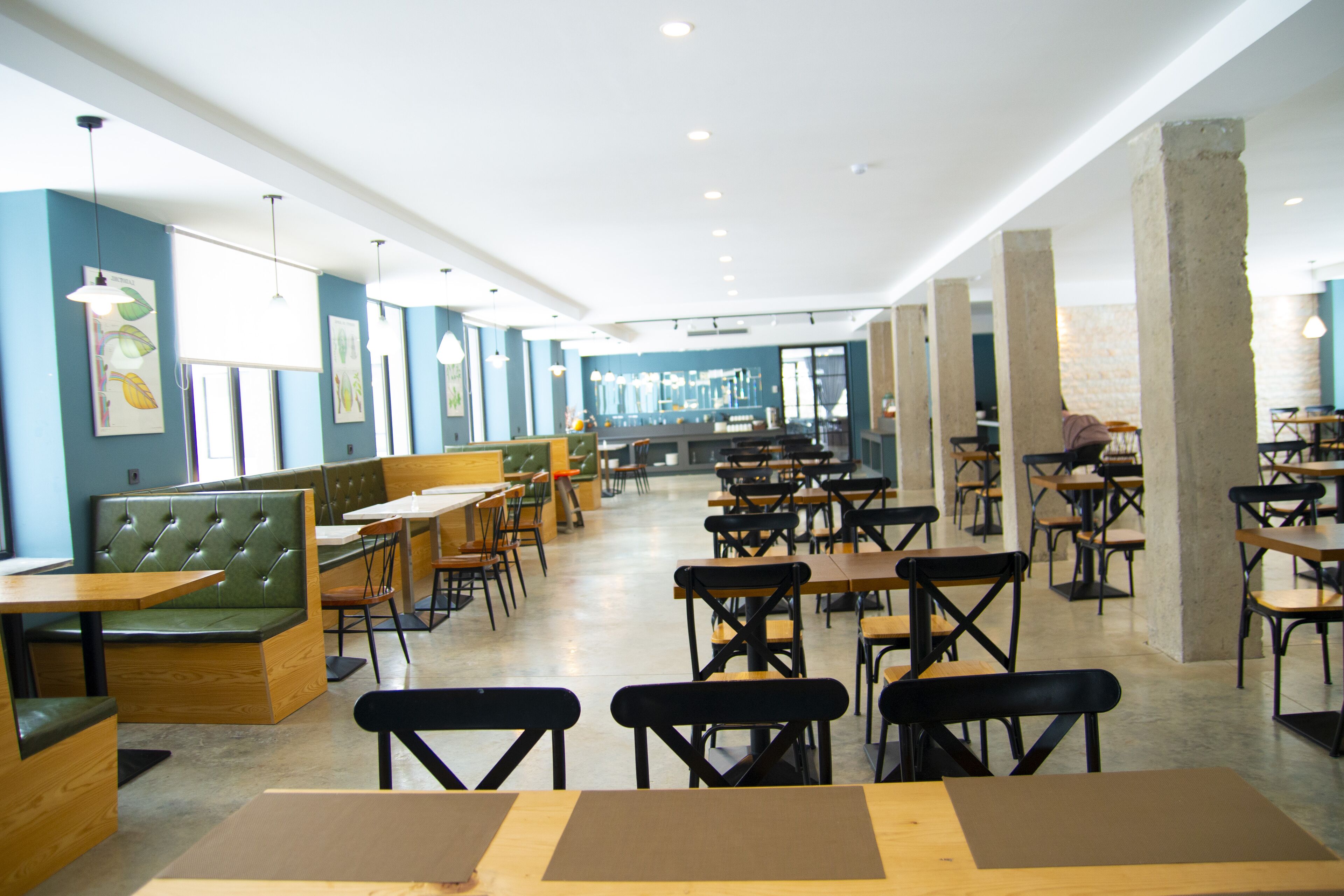 A spacious restaurant with high ceilings, green cushioned booths, and wooden tables and chairs.