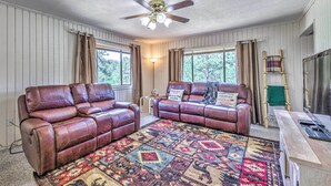 A living room with two leather sofas, a patterned rug, a ceiling fan, and a TV stand.