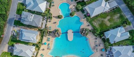 An aerial view of a resort with a central swimming pool, multiple villas, and a well-maintained landscape.
