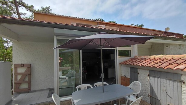 Eine Terrasse im Freien mit Tisch und Stühlen, eine Glastür zu einem überdachten Bereich und ein Ziegeldach.