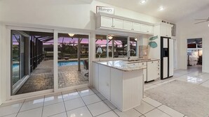 Et moderne køkken med en central ø, store vinduer og udsigt til et udendørs swimmingpool.