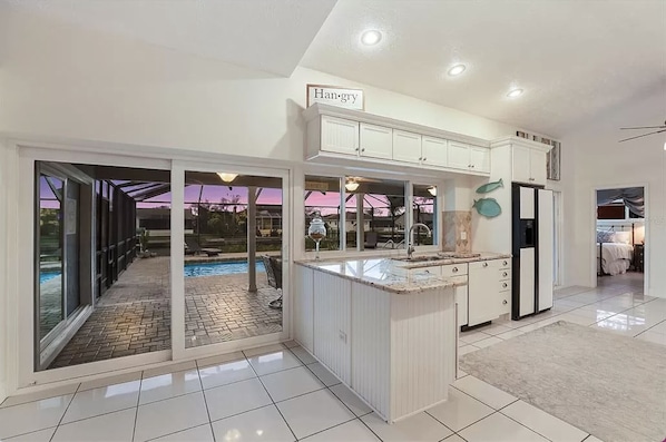 A modern kitchen with a central island, large windows, and a view of an outdoor swimming pool. - Seaside Oasis ~ Waterfront, Dog-Friendly, Saltwater Pool & Spa, Private Dock (Apollo Beach)