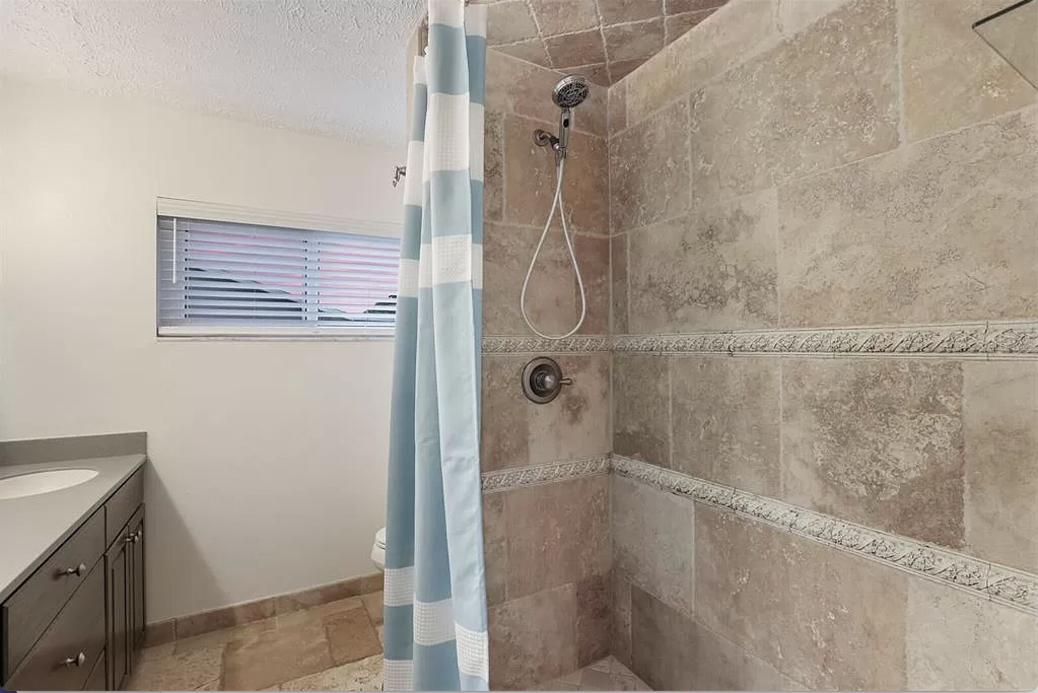Un baño con ducha, una ventana con persianas y un tocador con lavamanos.