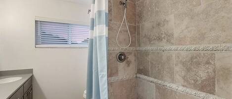 Un baño con ducha, una ventana con persianas y un tocador con lavamanos.