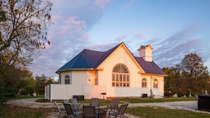 A large house with a blue roof and a chimney, surrounded by a gravel driveway and a grassy area with outdoor seating. - Dragonfly Inn (Only 40 min to Hocking Hills area) (Amanda)