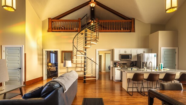 A spacious living area with a wooden staircase, a kitchen with a central island, and a dining area with bar stools. - Dragonfly Inn (Only 40 min to Hocking Hills area) (Amanda)