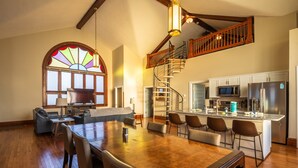 A spacious living room with a large wooden dining table, a staircase leading to an upper level, and a kitchen area with modern appliances. - Dragonfly Inn (Only 40 min to Hocking Hills area) (Amanda)