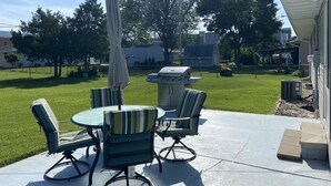 Une terrasse extérieure avec une table ronde et quatre chaises, un barbecue et un parasol.