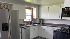 Une cuisine moderne avec des armoires blanches, un réfrigérateur en acier inoxydable, une cuisinière noire et une fenêtre avec un cadre en bois.