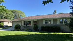 Une maison de plain-pied avec un porche à l’avant, un petit jardin et un ciel d’un bleu éclatant.
