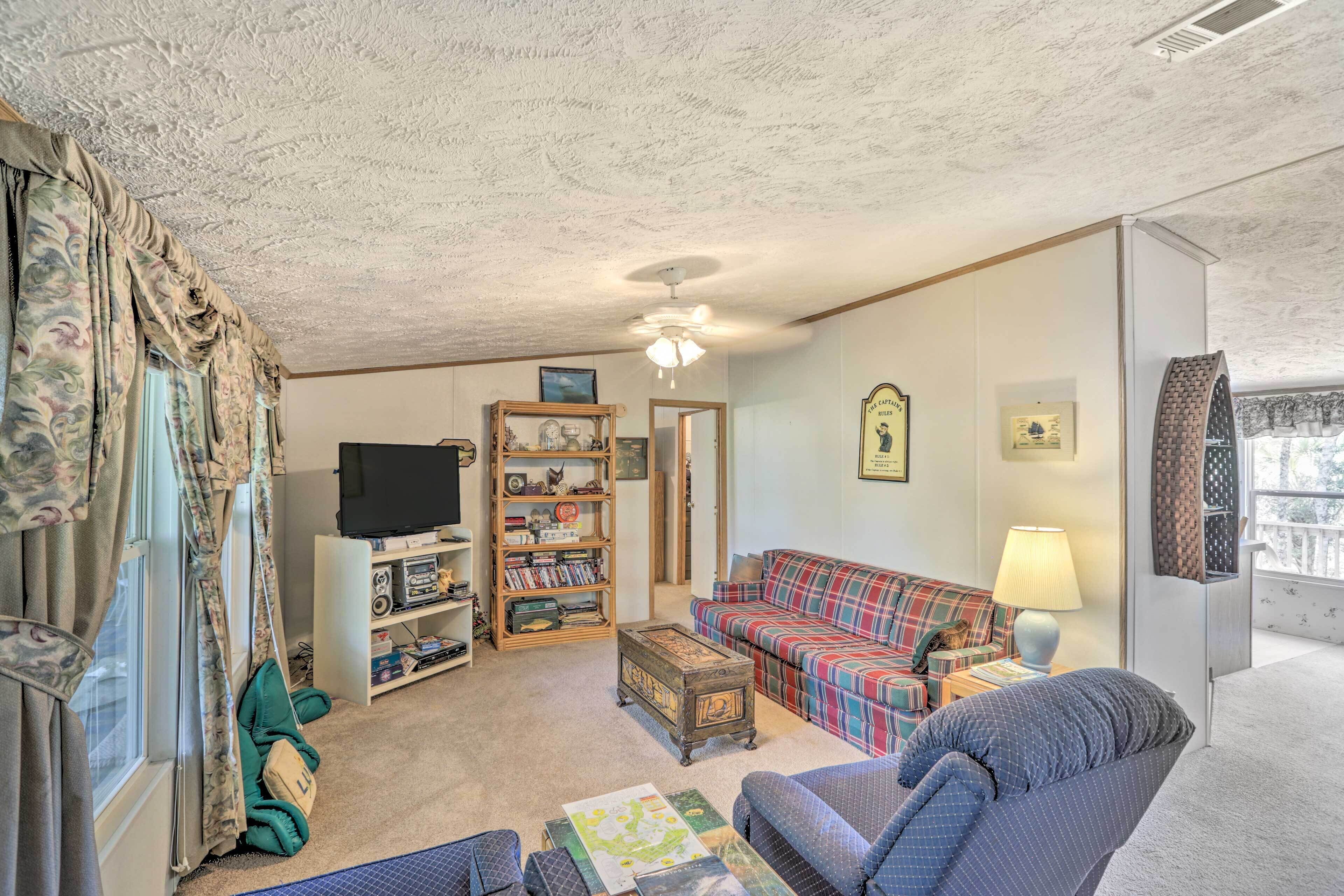 A cozy living room with a plaid sofa, a television, a bookshelf, and a ceiling fan.