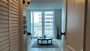 A hallway leading to a balcony with a view of a building. There is a table with a rug in the center of the balcony. - Beach front home away from home (Daytona Beach)
