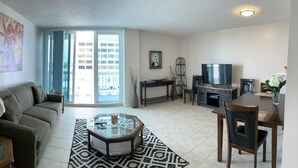 A living room with a sofa, coffee table, TV, and dining area. - Beach front home away from home (Daytona Beach)