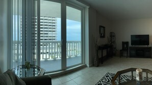 A living room with a large sliding glass door leading to a balcony, a television, and a fireplace. - Beach front home away from home (Daytona Beach)