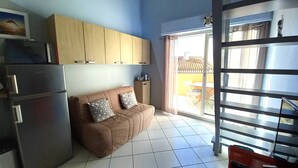 A compact living space with a kitchenette, a brown sofa with patterned cushions, and a sliding glass door leading to an outdoor area.
