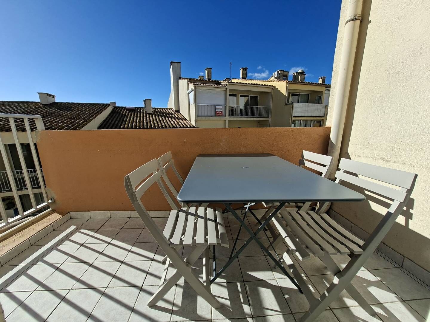 A small outdoor patio with a table and chairs, a tiled floor, and a view of neighboring buildings.