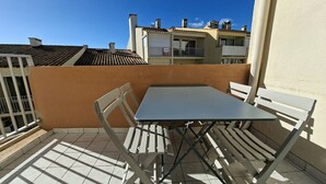A small outdoor patio with a table and chairs, a tiled floor, and a view of neighboring buildings.