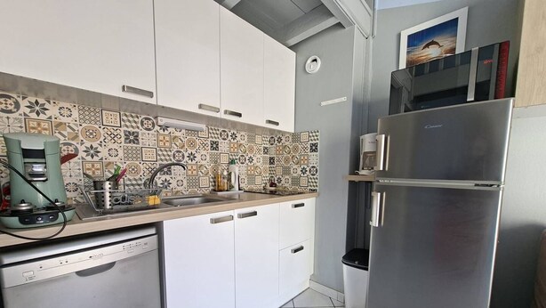 A compact kitchen with white cabinets, a stainless steel refrigerator, a coffee maker, and a tiled backsplash.