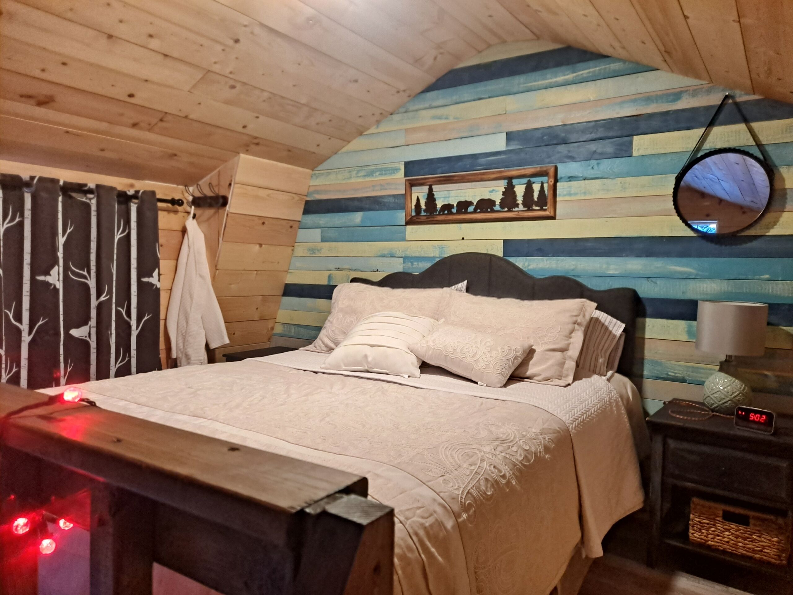 Et hyggeligt soveværelse med trælofter, en seng med hvide sengetæpper, et sengebord med en lampe og et spejl monteret på væggen.