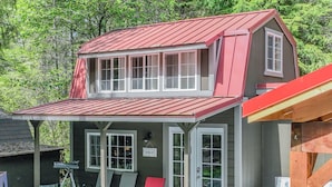 A two-story cabin with a red roof, a covered porch with chairs, and a telescope. - Tiny Home A, just steps from Mt. Rainer Nat. Park w/firepit. (Ashford)