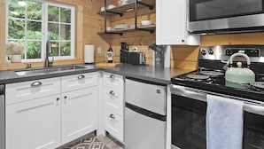 A modern kitchen with white cabinets, a stainless steel stove, and a microwave. - Tiny Home A, just steps from Mt. Rainer Nat. Park w/firepit. (Ashford)