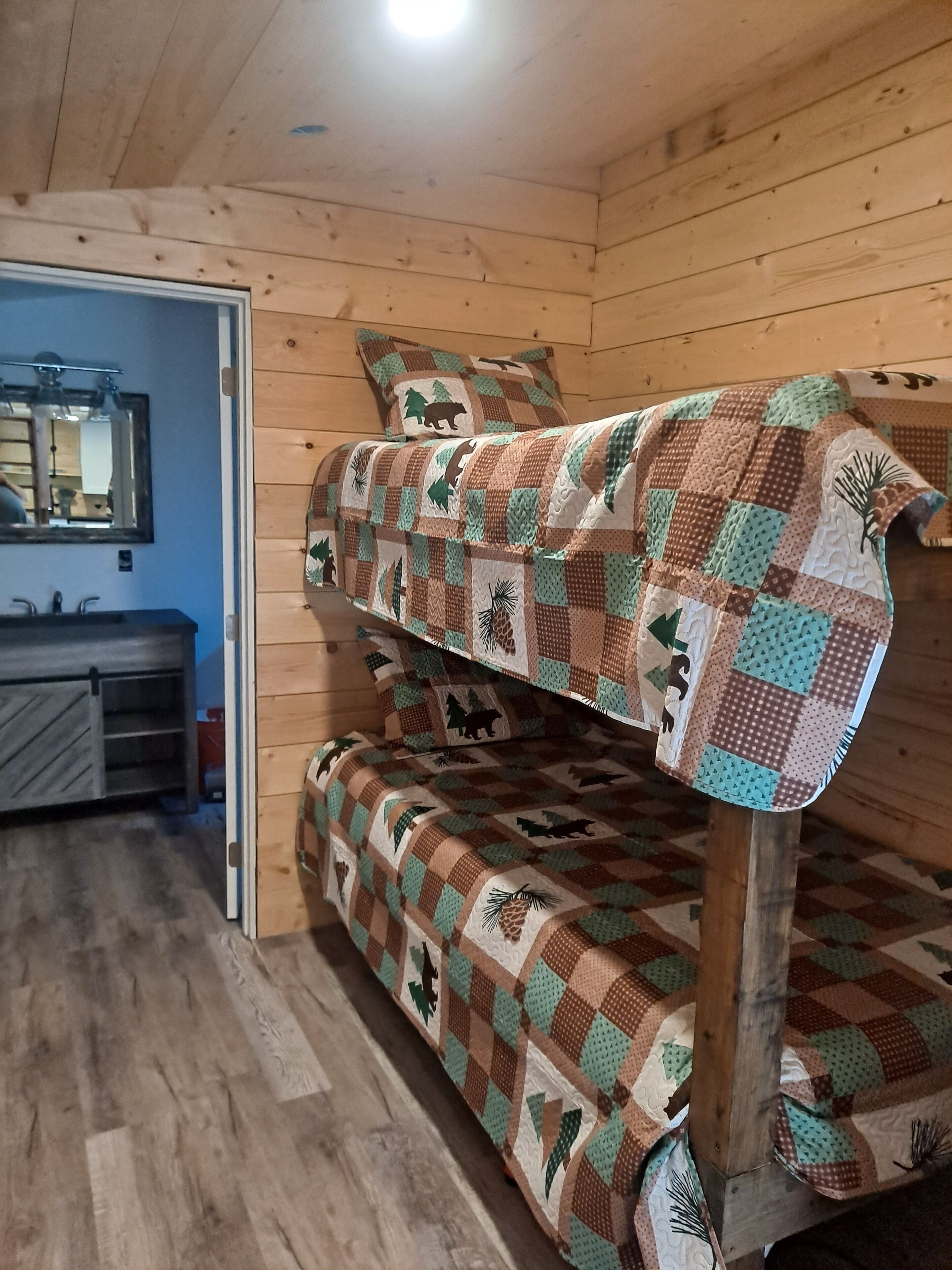 A bunk bed with a patchwork quilt, wooden walls, a mirror, and a sink.