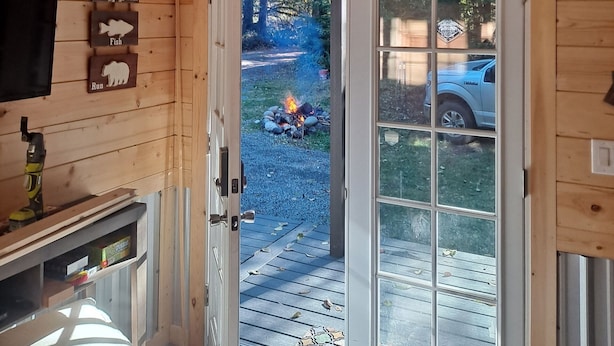 A wooden cabin interior with a television, a fireplace, and a door leading outside. - Tiny Home A, just steps from Mt. Rainer Nat. Park w/firepit. (Ashford)