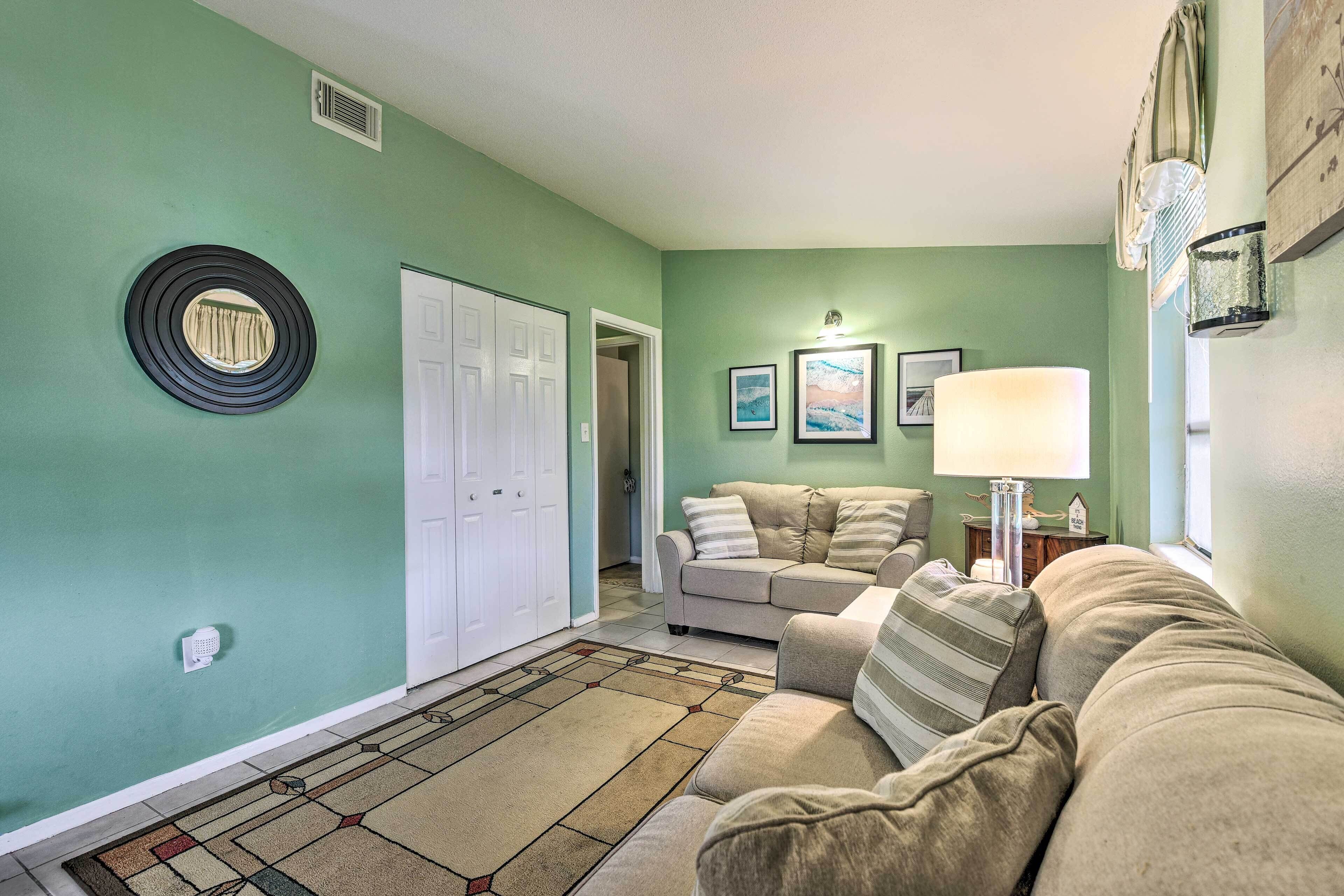 A living room with a beige sofa, a patterned rug, a white door, and a wall-mounted lamp.